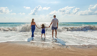 Mom, dad, and daughter holding hands while walking towrds the beach